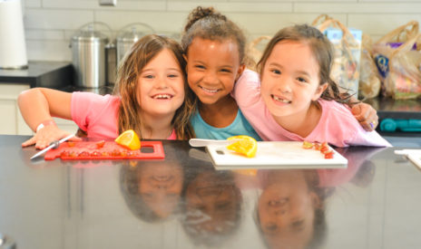 Three girls smiling at a kitchen counter while cooking