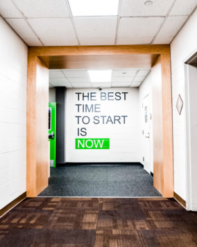 Entrance to the gym with a wall that has the quote "the best time to start is now"