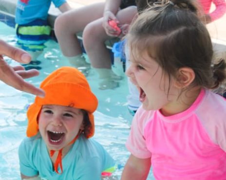 Two young children swimming in a pool at the Preschool Summer Camps (Infants-PreK) program