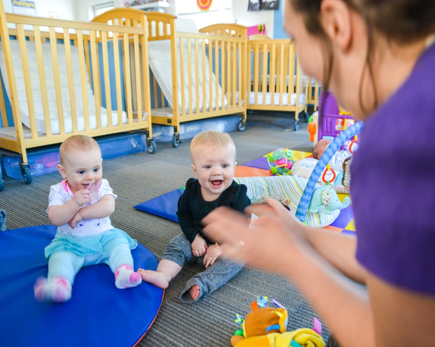 Two babies laughing with a teacher at the Preschool Vacation Camp